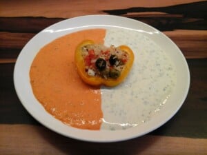 gefüllte Paprika auf dem Teller in einem Spiegel aus Paprika-Soße mit und Tsatsiki